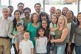 Group of diverse people of various ages smiling and posing together in a brightly lit indoor setting.